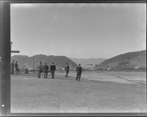 Group of unidentified men, watching an Auster airplane land at Greymouth airport, during the Auster tour
