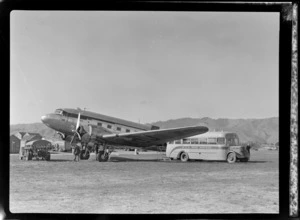 View of NZ NAC (National Airways Corporation) Dakota ZK-AOJ transport plane with a NZR Road Services bus and Shell Oil trucks at Paraparaumu Airfield, Wellington Region