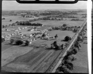 View to a large group of [dormitory?] wooden buildings of a [camp, school or military base?] with playing field and pool, surrounded by farmland, Levin District, Manawatu-Whanganui Region