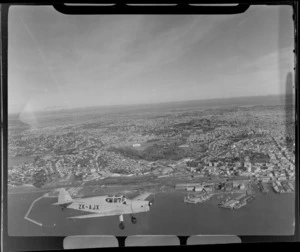 Auckland Aero Club's DH94 Moth Minor KZ-AJX plane in flight over Auckland City with the waterfront and Auckland Domain in view