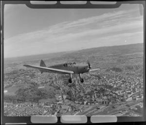 Auckland Aero Club's DH94 Moth Minor KZ-AJX plane in flight over Auckland City with the railway yards and Auckland Domain in view