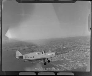 Auckland Aero Club's DH94 Moth Minor KZ-AJX plane in flight over Auckland Harbour with Auckland City and waterfront in view