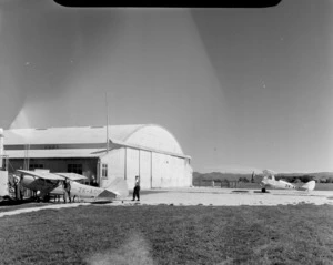 Auster ZK-AOB airplane and unidentified men, outside a hangar, Gisborne airport, including a ZK-ANF airplane