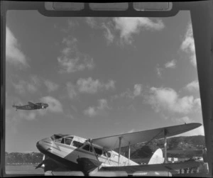 A grounded De Havilland Dominie 'Tawaka' airplane and a Lockhead Lodestar in flight, NZNAC (New Zealand National Airways Corporation) [Wellington?]