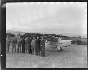 Portrait of unidentified men, including two in military style uniforms, in front of Auster J-1B Autocrat ZK-AOB passenger plane, Gore, Southland Region