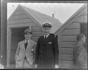 Portrait of former pilot D Campbell and NZ NAC (National Airways Corporation) pilot G Harvey in uniform in front of sheds, Invercargill District, Southland Region