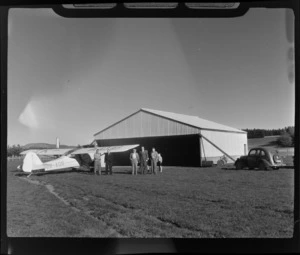 Unidentified Waipukurau Aero Club members with Auster J/1Autocrat ZK- AOB aeroplane in front of a hangar, Waipukurau District, Central Hawke's Bay Region