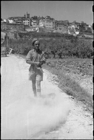 W L Hennesy repairing vital wire link on dusty road between Castiglione and Lignano, Italy, during World War II - Photograph taken by George Kaye