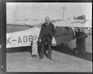 Mr A McIntosh with a small child, in front of an Auster ZK-AOB airplane, Invercargill