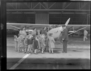 Unidentified man showing young school children an Auster airplane, accompanied by three unidentified women, Rongotai airport, Wellington