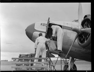 Two unidentified ground staff, unloading baggage from cargo hold of aircraft 'Kotare', at Harewood Aerodrome (Christchurch International Airport)