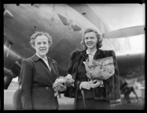 Passengers Mrs B W A Dickson (left) and Mrs M Summers, passengers on a Vickers Armstrong aeroplane, holding flowers presented to them on their arrival at Whenuapai Airbase, Auckland