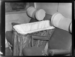 Interior of a Tasman Empire Airways Ltd flying boat, showing a basinette placed between passenger seats, probably in first class cabin area