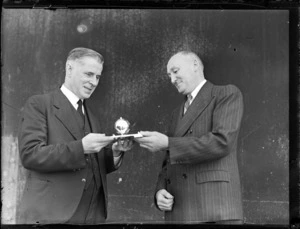 The Honourable F Jones, left, holding a trophy, with Mr AW Coles, at opening of British Commonwealth Pacific Airlines' trans Pacific service, Whenuapai Airport, Auckland