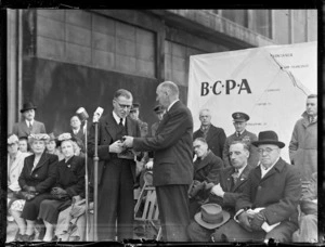 The Honourable F Jones, left, with Mr AW Coles, right, in front of a crowd at the opening ceremony for British Commonwealth Pacific Airlines' trans Pacific service, Whenuapai Airport, Auckland