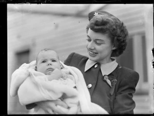 Joan Hutchens, stewardess for Trans Australian Airlines, holding an infant who has been travelling onboard