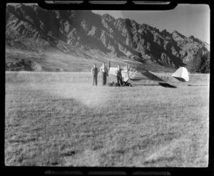 D [Grieg?], Leo White, and T Ewart, standing next to an Auster Autocrat monoplane, ZK-AOB, with The Remarkables in background, Queenstown, Otago Region