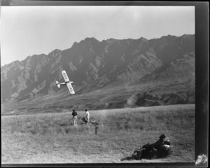 Auster Autocrat aeroplane, ZK-AOB, flying low over a field, as three unidentified children watch from the ground, Queenstown, Otago Region