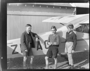 Three boys; Mal Greenslade, left, Brian Soutes, and Ian Soutes, standing alongside Auster Autocrat aeroplane, ZK-AOB, [Dunedin?]