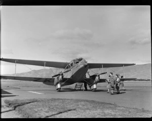 View of unidentified passengers disembarking NZ NAC ((National Airways Corporation) De Havilland Dominie 'Tara' bi-plane ZK-AKS at Omaka Airport, Blenheim, Marlborough Region