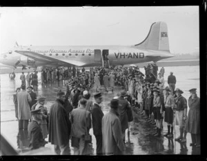 British Commonwealth Pacific Airlines inugural trans Pacific flight to Vancouver, showing passengers boarding Douglas Skymaster DC-4 aeroplane 'Tatana', VH-AND, with crowd, including Scouts, lined up on tarmac, Whenuapai Airport, Auckland
