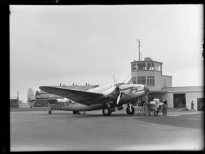 NZ NAC ((National Airways Corporation) Lockheed 18-56 Lodestar aeroplane 'Kotuku' ZK-AIQ being loaded by an unidentified man in front of the Harewood Airport control tower, Christchurch City, Canterbury Region