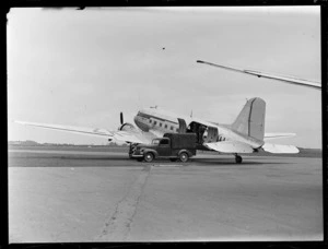 View of a Dakota transport plane with two unidentified men unloading goods on to a truck at Harewood Airport, Christchurch City, Canterbury Region
