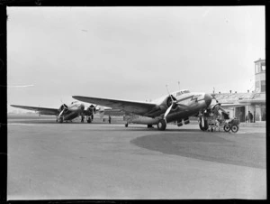 View of NZ NAC ((National Airways Corporation) Lockheed 18-56 Lodestar aeroplanes 'Kotuku' ZK-AIQ and 'Kawatere' ZK-ANA with unidentified ground crew in front of the control tower at Harewood Airport, Christchurch City, Canterbury Region