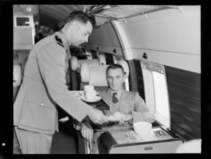 View of an unidentified male passenger being served tea by an unidentified steward on visiting British Vickers Viking passenger plane G-AJJN