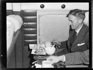 Portrait of an unidentified man sitting in visiting British Vickers Viking passenger plane G-AJJN showing the use of an auxiliary table while seated