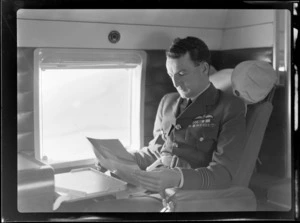 Portrait of Squadron Leader J Steele on board visiting British Vickers Viking passenger plane G-AJJN reading advertising material