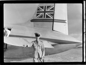 Portrait of an unidentified [TEA Stewart?], in uniform, from the visiting British Vickers Viking passenger plane G-AJJN standing in front of the plane's tail wing, [Whenuapai Airport, Auckland City?]