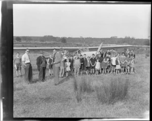 Unidentified men and a group of [school?] children, in front of an Auster airplane, Balclutha, Southland