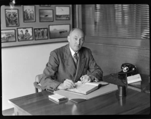 Portrait of Sir Arthur William Coles, of TAA (Trans Australia Airlines), sitting at desk, writing in book