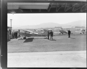 Aircraft ZK-AOB Auster J1B Aiglet, including other aircrafts and unidentified people watching aircraft Lockhead Lodestar ZK-AHX 'Karoro', at Taieri airport and aerodrome, Dunedin, Otago region