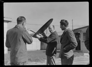 Portrait of (L to R) TEAL employees Mr K A Brownjohn, Mr C Griffiths and Mr F D Bathwaite examining a model aircraft wing, [Mechanics Bay, Auckland City