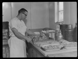 Portrait of an unidentified male TEAL Catering Staff member with a tray of cooked chickens within the kitchen of an unidentified building, [Auckland?]