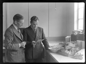 View of (L to R) Mr Eric Mullane, TEAL Catering Officer, with an unidentified man looking at a food list within a kitchen at Mechanics Bay, Auckland City