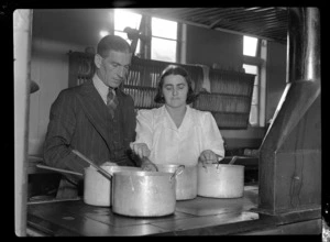 View of Mr Eric Mullane, TEAL Catering Officer, supervising an unidentified woman cooking, Mechanics Bay, Auckland City