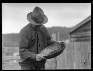 Goldmining, view of old 'beachcomber' [Ted Bagley?] panning for gold on a South Westland beach, West Coast Region