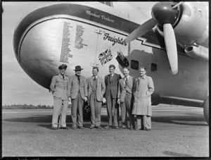 Group portrait of crew members under the nose cone with names of airports visited of the visiting Bristol Freighter transport plane 'Merchant Venturer' G-AIMC, Whenuapai Airfield, Auckland