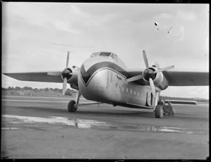 View of visiting Bristol Freighter transport plane 'Merchant Venturer' G- AIMC with unidentified men unloading baggage from a side door, Whenuapai Airfield, Auckland