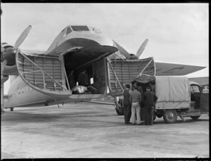 Unidentified men loading truck from front cargo bay of visiting Bristol Freighter transport plane 'Merchant Venturer' G-AIMC, Whenuapai Airfield, Auckland City