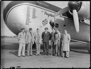 Group portrait of Mr N Higgs with crew members off the visiting Bristol Freighter transport plane 'Merchant Venturer' G-AIMC with names of airports visited on front cargo door, Whenuapai Airfield, Auckland