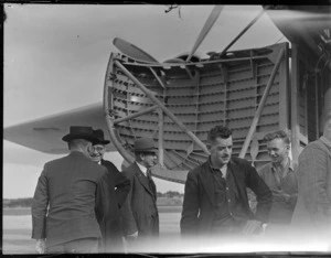 View of unidentified men in front of visiting Bristol Freighter transport plane 'Merchant Venturer' G-AIMC with front cargo doors open, Whenuapai Airfield, Auckland City
