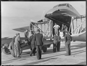 Unidentified civilian and military men loading military equipment in to front cargo bay of visiting Bristol Freighter transport plane 'Merchant Venturer' G-AIMC, Whenuapai Airfield, Auckland City