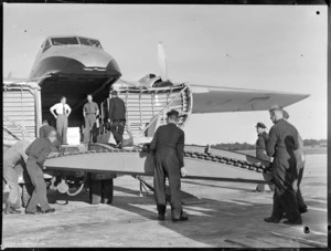 Unidentified civilian and military men assembling loading ramps into front cargo bay of visiting Bristol Freighter transport plane 'Merchant Venturer' G-AIMC, Whenuapai Airfield, Auckland City