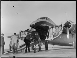 View of Mr Higgs' car being driven into the front cargo bay of visiting Bristol Freighter transport plane 'Merchant Venturer' G-AIMC with unidentified men looking on, Whenuapai Airfield, Auckland City
