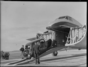 View of Mr Higgs' car being driven into the front cargo bay of visiting Bristol Freighter transport plane 'Merchant Venturer' G-AIMC with unidentified men looking on, Whenuapai Airfield, Auckland City