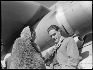 Bristol Freighter tour, Rotorua, showing Mr F E Sanders receiving a poi brooch from Guide Rangi, who is wearing a Maori cloak and a headscarf, standing beside a Bristol Freighter aircraft